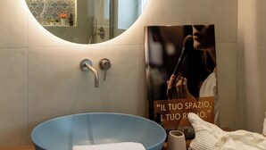 Un baño con un espejo redondo, un lavabo azul y una toalla en la encimera.
