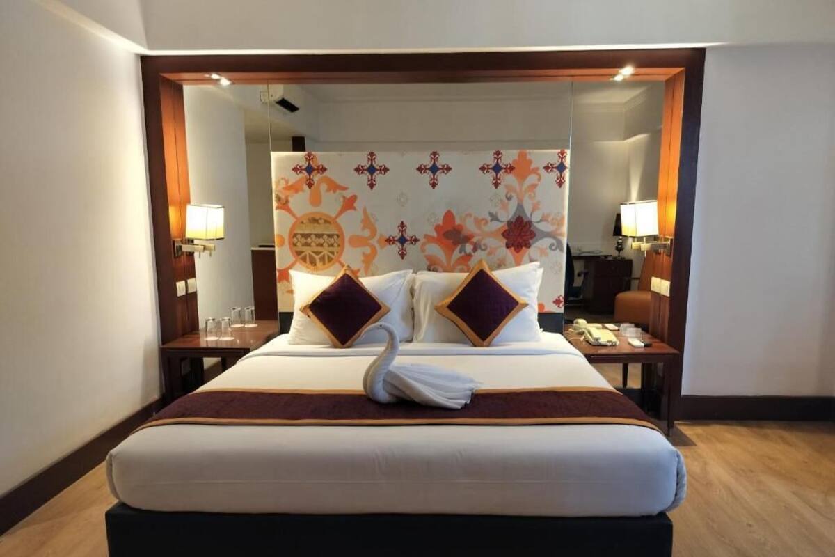 Una habitación de hotel con una cama grande, dos mesitas de noche, un espejo y un cabecero decorativo.