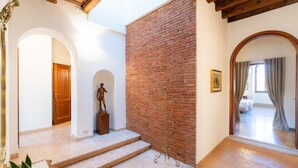 Un interior amplio con pared de ladrillo, una estatua y una escalera que lleva a otra habitación.