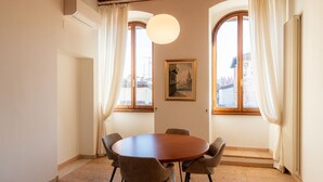 Comedor con una mesa redonda, cuatro sillas, una lámpara colgante y dos ventanas con cortinas.