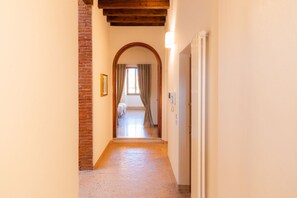 A hallway with a brick wall, wooden ceiling beams, and a door leading to a room with a bed and curtains. - Elegant estate overlooking Piazza Erbe (Verona)