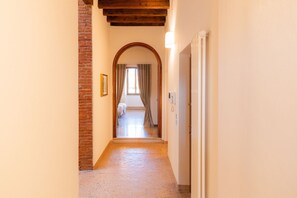 A hallway with a brick wall, wooden ceiling beams, and a door leading to a room with a bed and curtains. - Noble residence overlooking Piazza Erbe (Verona)