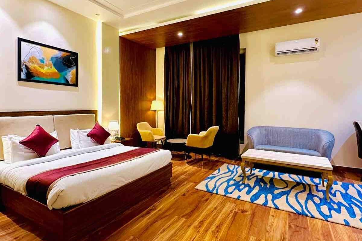 A hotel room with a bed, a desk, two chairs, a ceiling fan, and an air conditioning unit.