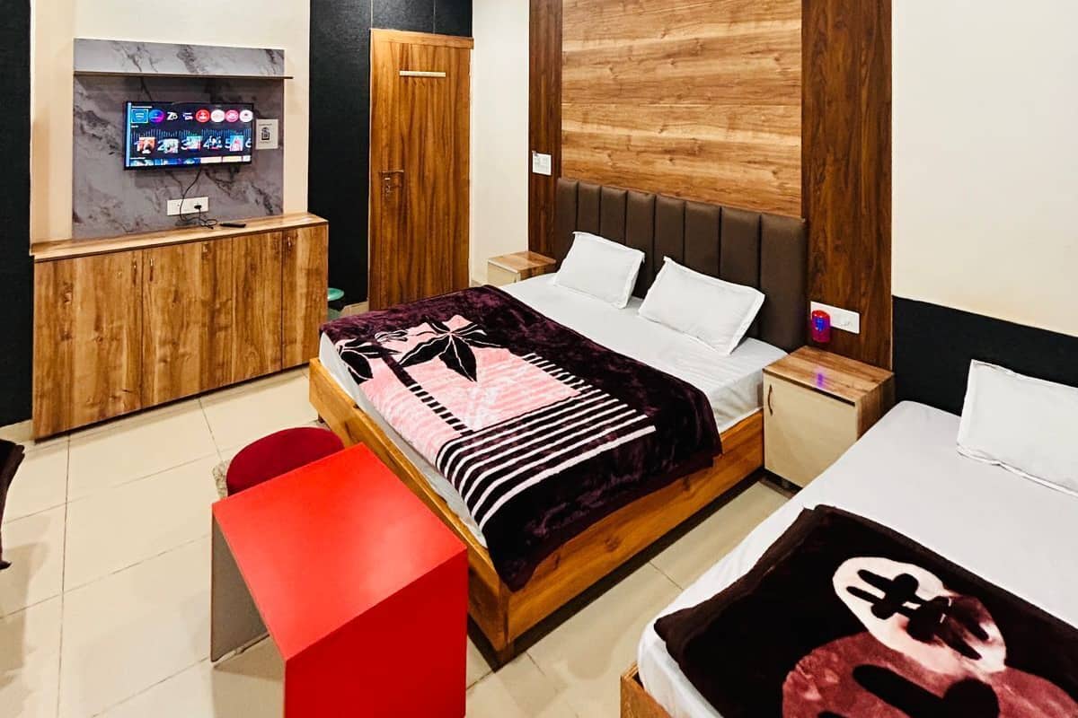 A modern hotel room with a bed, a TV, a wooden accent wall, and a red bench.