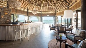 A bar area with a stone wall, white chairs, and a view of the ocean. - Veranda Paul et Virginie Hotel and Spa - Adults Only (Grand Gaube)