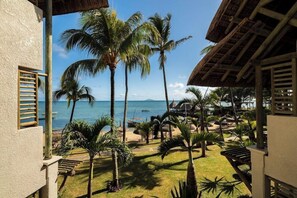 A resort with a view of the ocean, palm trees, and thatched-roof structures.