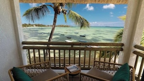 A balcony with wicker furniture, a small table, and a view of a beach with boats and palm trees. - Veranda Paul et Virginie Hotel and Spa - Adults Only (Grand Gaube)