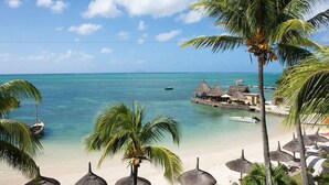 A beach with clear turquoise water, a thatched-roof structure, and palm trees. - Veranda Paul et Virginie Hotel and Spa - Adults Only (Grand Gaube)