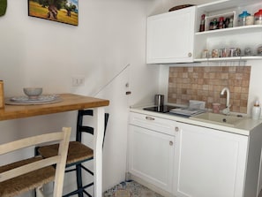 Una cocina compacta con una mesa de madera, una silla, un lavamanos y un armario con espacio de almacenamiento.