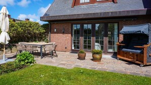 Een huis met een terras, een eettafel, stoelen, een barbecue en potplanten.
