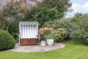 Ein Garten mit einer Holzterrasse, einem gestreiften Baldachin und einem Blumentopf.