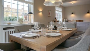 Een eetgedeelte met een lange houten tafel, gedekt voor een maaltijd, een groot raam met uitzicht en een moderne hanglamp.
