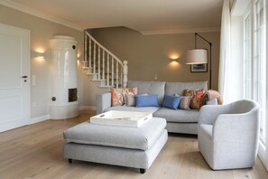 A living room with a grey sofa, ottoman, and armchair, a staircase, and a white door.