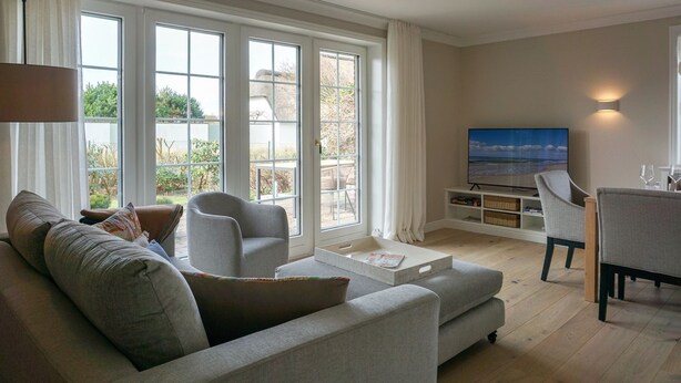 Een woonkamer met een bank, fauteuil, salontafel, televisie en een eethoek met stoelen.
