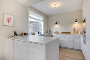 A modern kitchen with white cabinetry, a large island, a window with a view, and pendant lighting. - Inselhüs - Inselhüs on Sylt: family-friendly, 150 m², wood-burning stove & (Wenningstedt-Braderup (Sylt))
