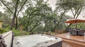 Un jacuzzi en una terraza de madera con mobiliario exterior y una zona cubierta.