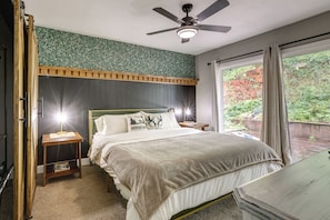 A bedroom with a bed, bedside tables, a ceiling fan, a window with curtains, and a view of greenery outside. - Placerville Paradise: Game Room + Hot Tub! (Placerville)