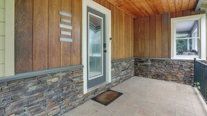 Un porche cubierto con paredes de madera, un detalle de pared de piedra y una puerta con panel de vidrio esmerilado.