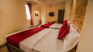 A hotel room with two beds, each with red and white bedding, a wooden headboard, a television on the wall, and a window with curtains. - Hotel Vichar Vimarsh (Darjeeling)