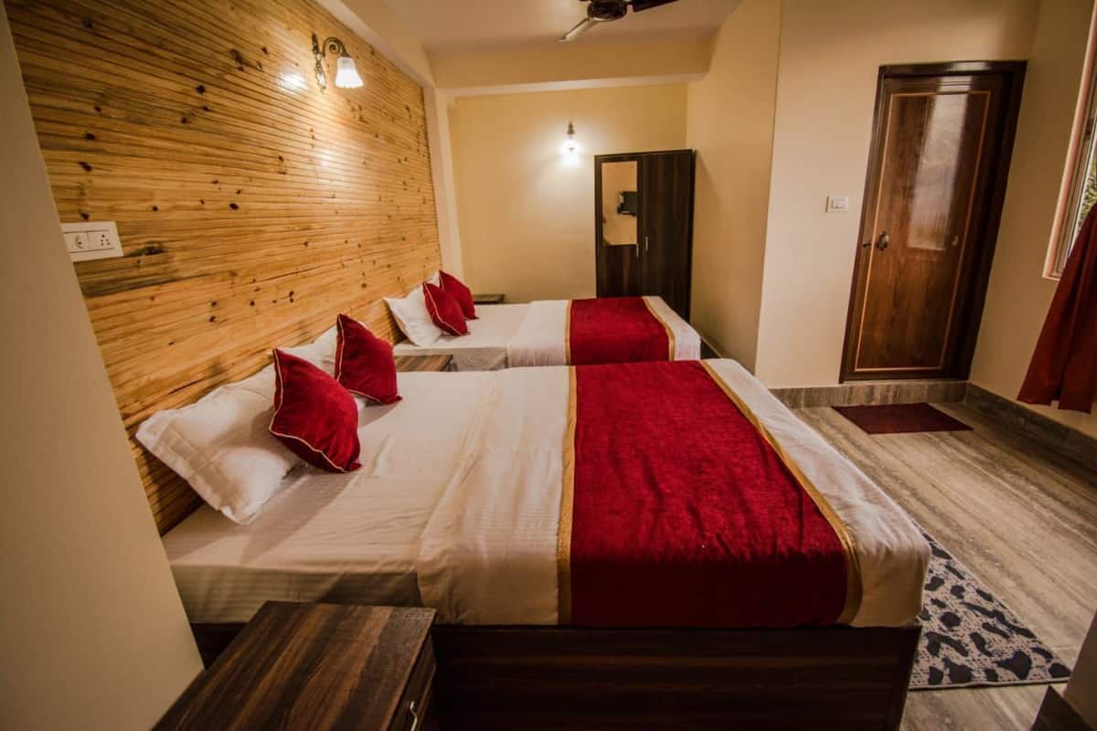 A hotel room with four beds, wooden headboard, a wardrobe, and a small table.