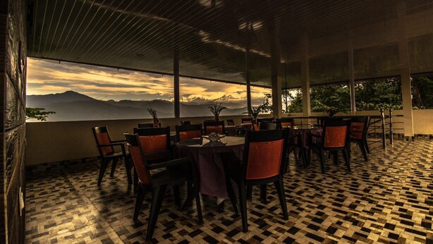 A restaurant with a checkered floor, tables with chairs, and a view of mountains. - Hotel Vichar Vimarsh (Darjeeling)