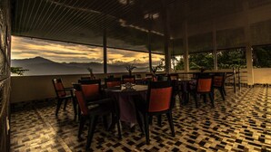 An outdoor dining area with tables and chairs, a patterned floor, and a view of mountains. - Hotel Vichar Vimarsh (Darjeeling)