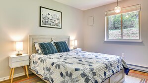 Un dormitorio con una cama, dos mesitas de noche, una lámpara de noche, una ventana con vistas y un aplique de techo.