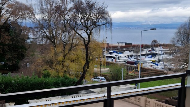 Ein Balkon mit Tisch und Stühlen, einer gemusterten Matte und Blick auf Boote und Bäume.