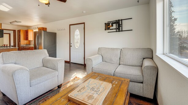Uma sala de estar com dois sofás, uma mesa de centro, um ventilador de teto, uma porta com painel de vidro decorativo e uma cozinha ao fundo.