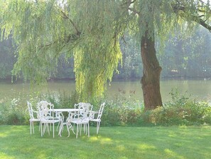 Ein Tisch mit Stühlen unter einem Baum am See.