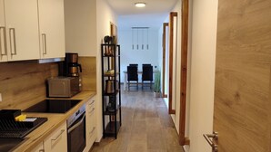 Et smalt køkken med moderne hårde hvidevarer, en træbordplade og et spiseområde med bord og stole.