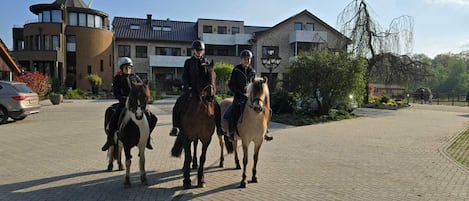 Three people riding horses on a paved area with buildings in the background.