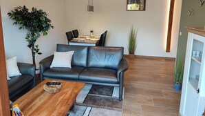 En moderne stue med en lædersofa, et spisebord dækket til fire personer, og et køkken i baggrunden.