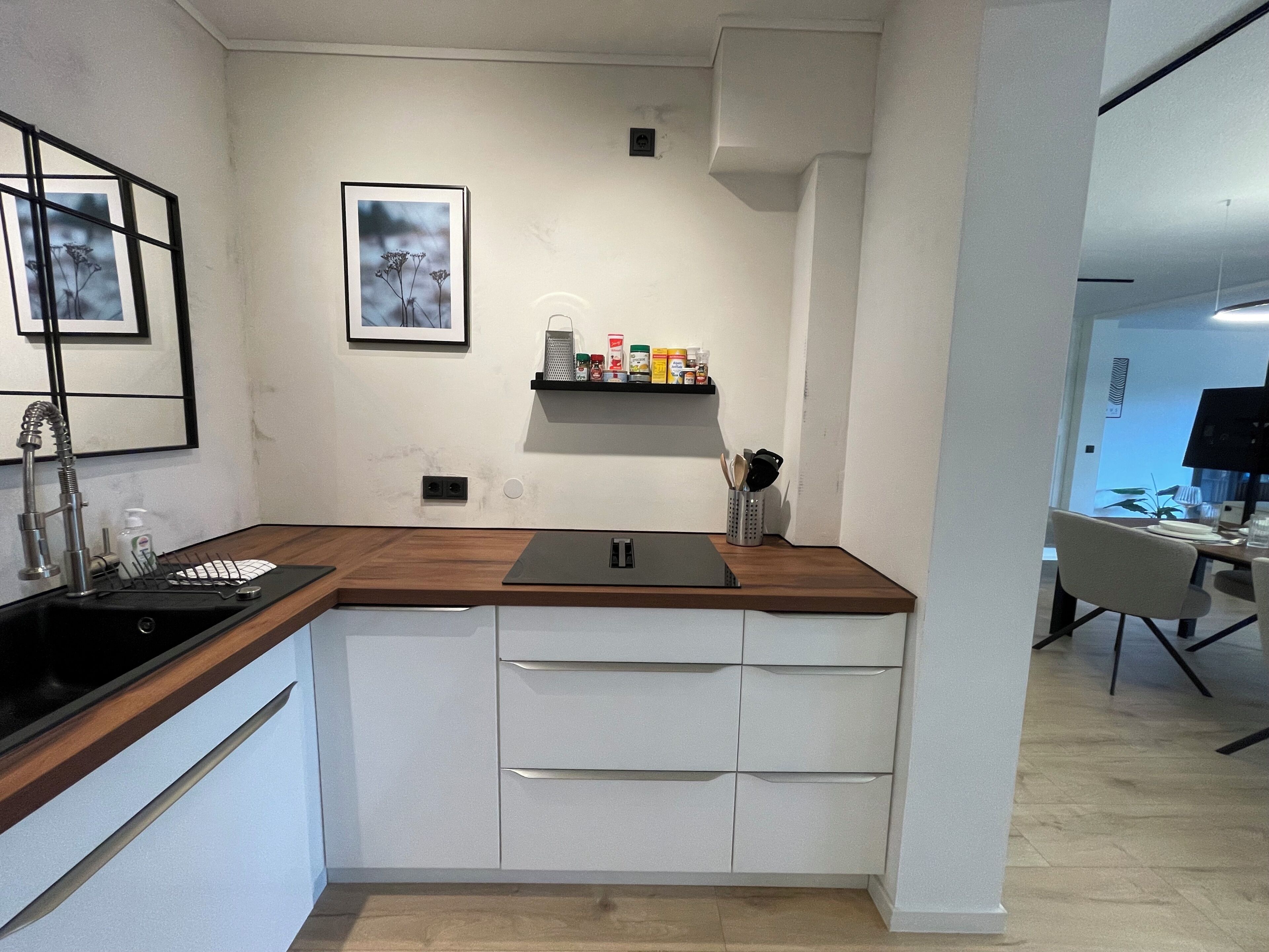 Una cocina moderna con encimera de madera, armarios blancos, un lavabo negro y un pequeño estante con utensilios de cocina.