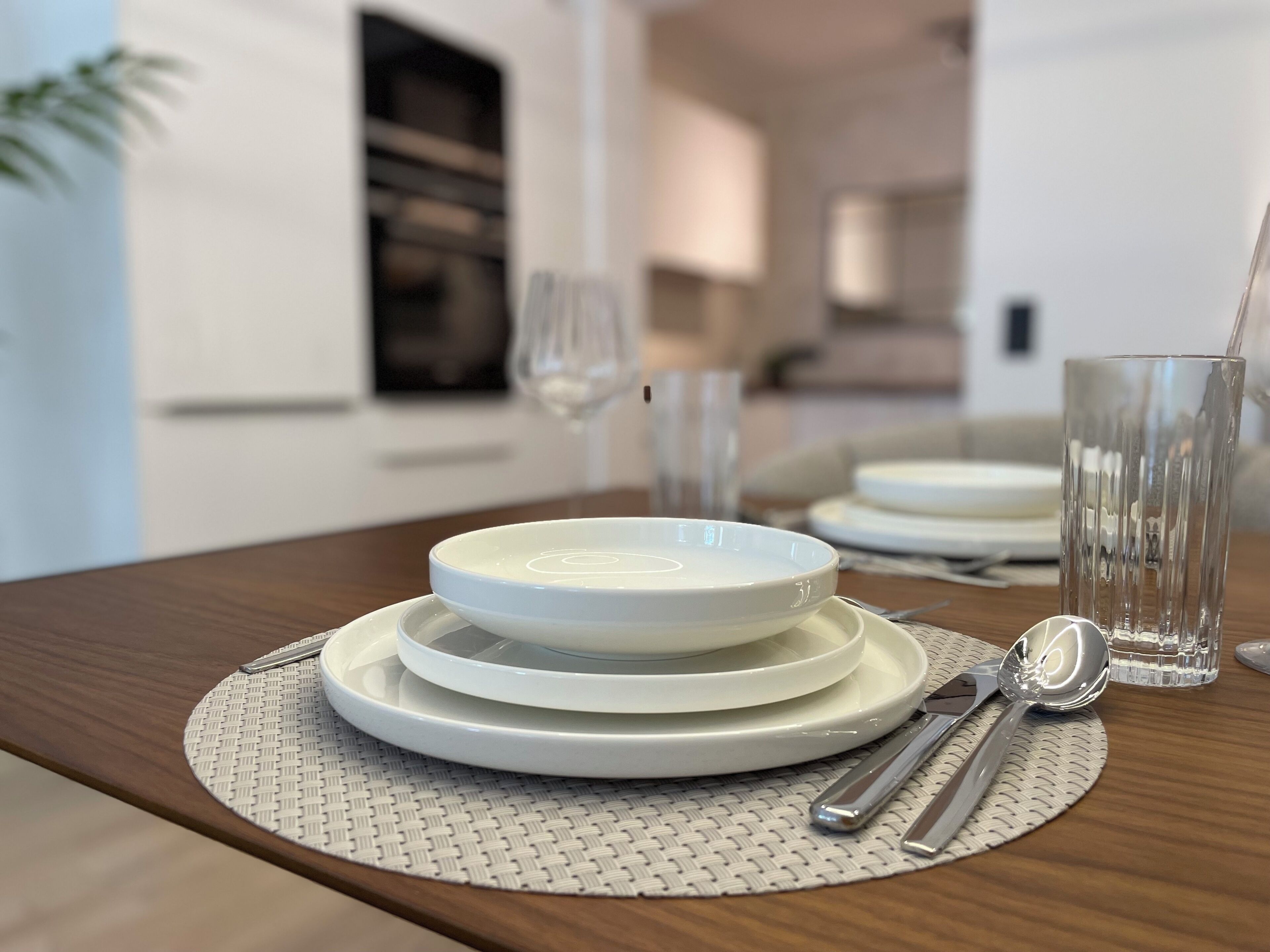 Une table à manger avec une pile d’assiettes blanches, un verre transparent et des couverts.