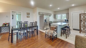 Uma cozinha moderna com uma ilha central, uma área de refeições com mesa de vidro e um espaço de estar com poltrona estampada.