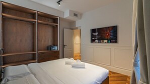 Une chambre à coucher avec un grand lit, une armoire, un téléviseur fixé au mur et une porte donnant sur une autre pièce.