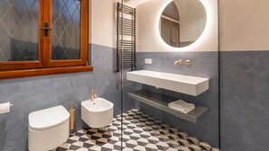 Une salle de bain équipée de toilettes, d’un bidet, d’un lavabo et d’un miroir à cadre rond.