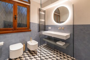 Ein Badezimmer mit Toilette, Bidet, Waschbecken und einem Spiegel mit rundem Rahmen.