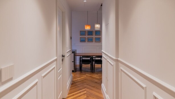 Un couloir doté d’un plancher en bois, de murs blancs et d’un coin repas avec une table et des chaises.