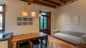 Un espace repas comprenant une table et des chaises en bois, un canapé et des luminaires suspendus.