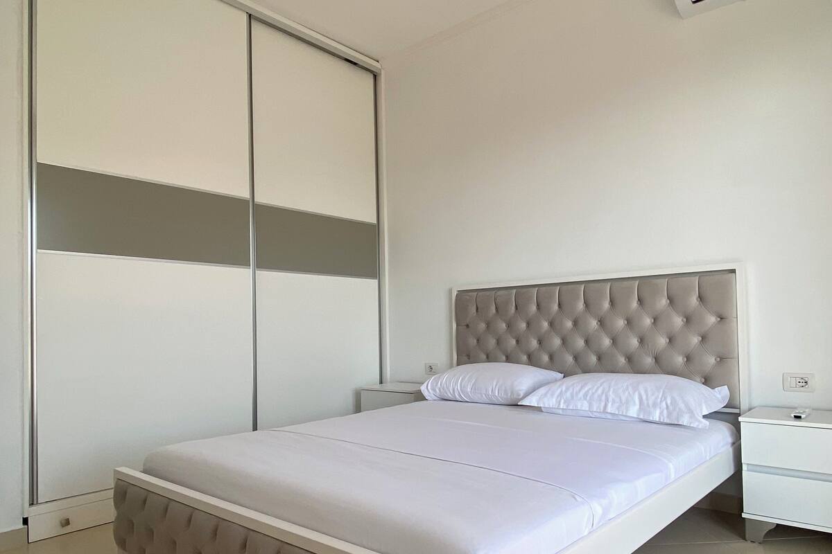 A bedroom with a bed, a nightstand, a wardrobe, and an air conditioning unit.
