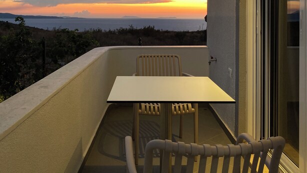 A balcony with a table and chairs, overlooking a sunset view.
