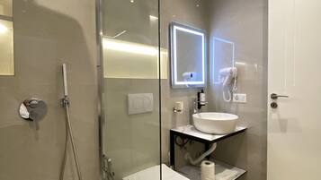 A modern bathroom with a glass shower enclosure, a toilet, a sink with a mirror, and a towel rack.