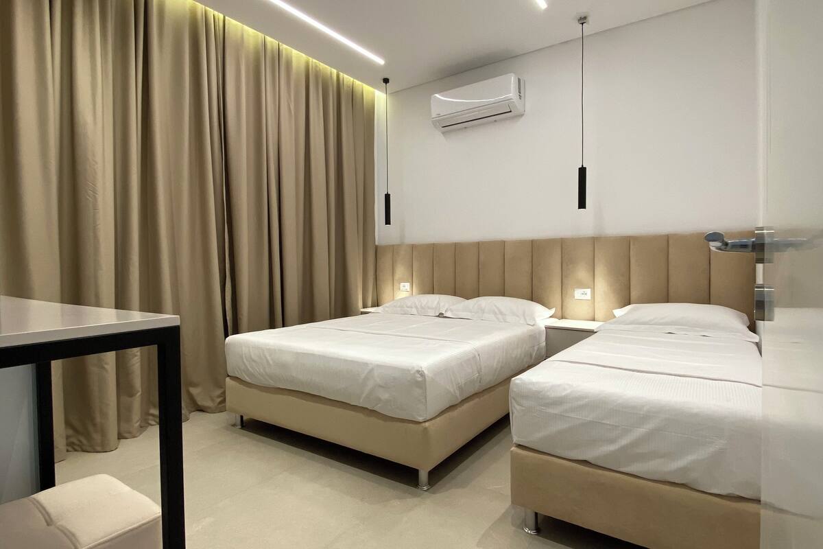 A hotel room with two beds, a table, and a modern ceiling light fixture.