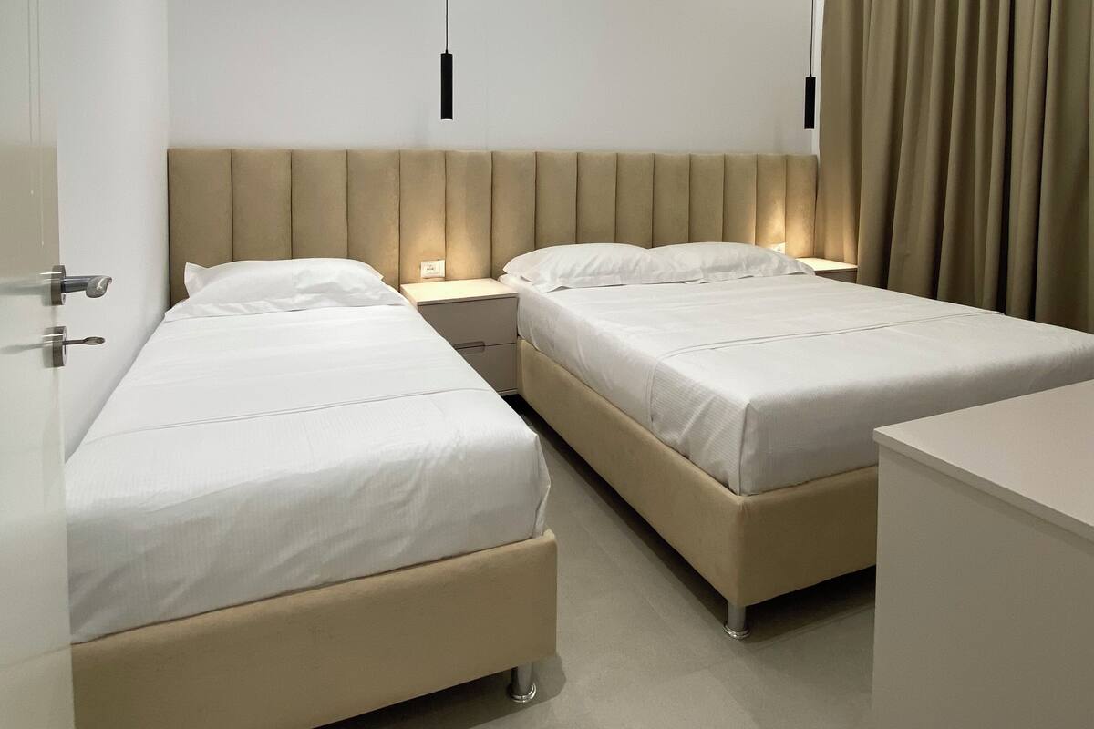 A modern hotel room with two beds, a nightstand, a desk, and a large window with curtains.
