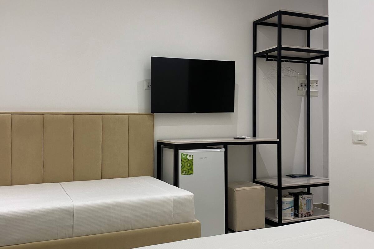 A modern hotel room with a bed, a flat-screen TV, a mini-fridge, and a built-in wardrobe.