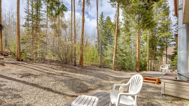 Eine Terrasse mit zwei weißen Stühlen, einem Grill und Blick auf einen Wald.