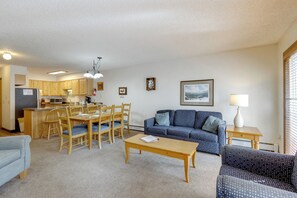 Ein Wohnzimmer mit einer Couch, Couchtisch, Esstisch, Stühlen, einer Küchenzeile und einem gerahmten Bild an der Wand.