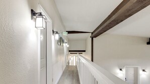Ein Korridor mit weißen Wänden, einem Holzbalken an der Decke und einem weißen Geländer.